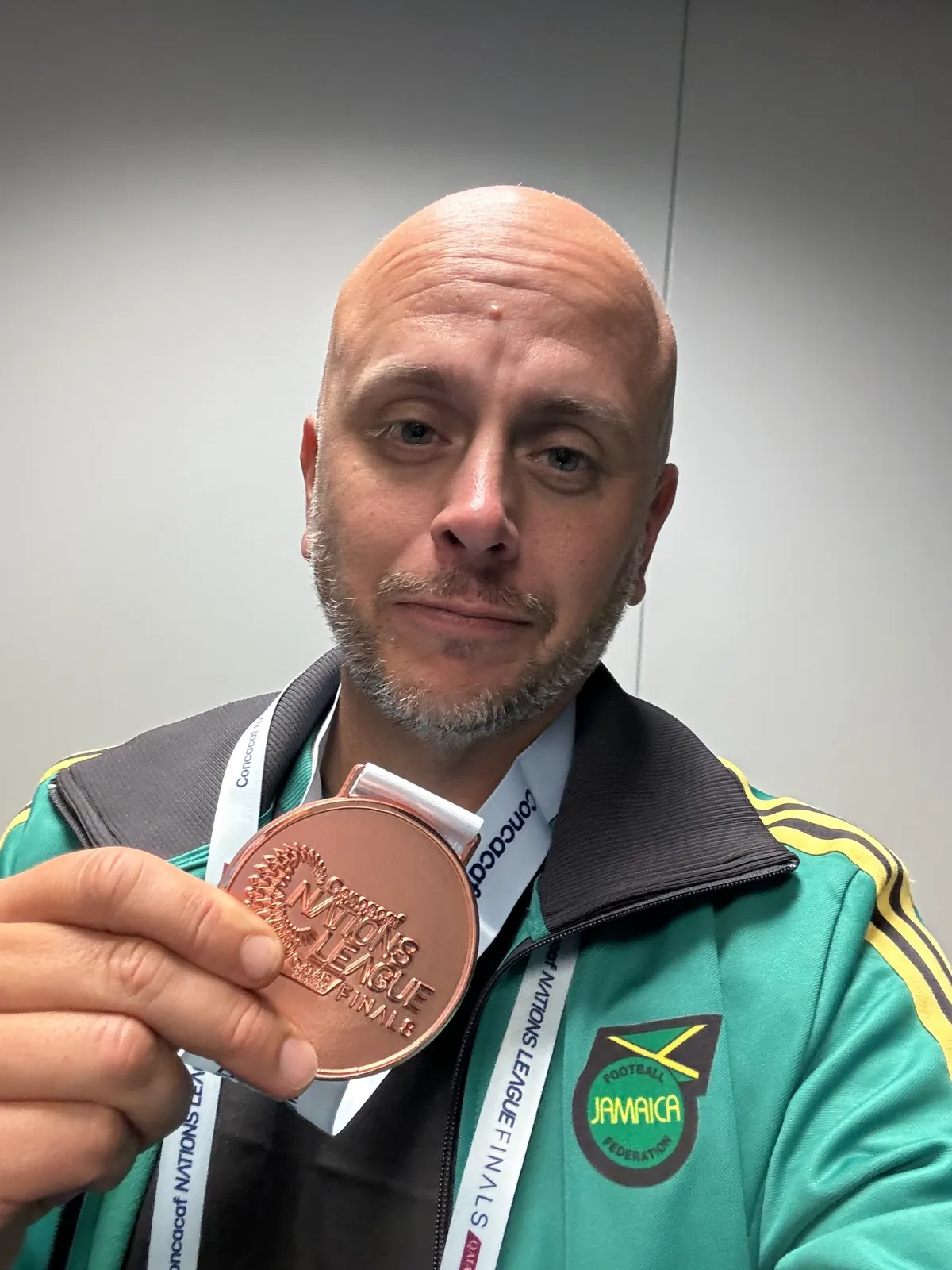 John Wall in a Jamaica Football Federation jacket holding a Concacaf Nations League Finals bronze medal