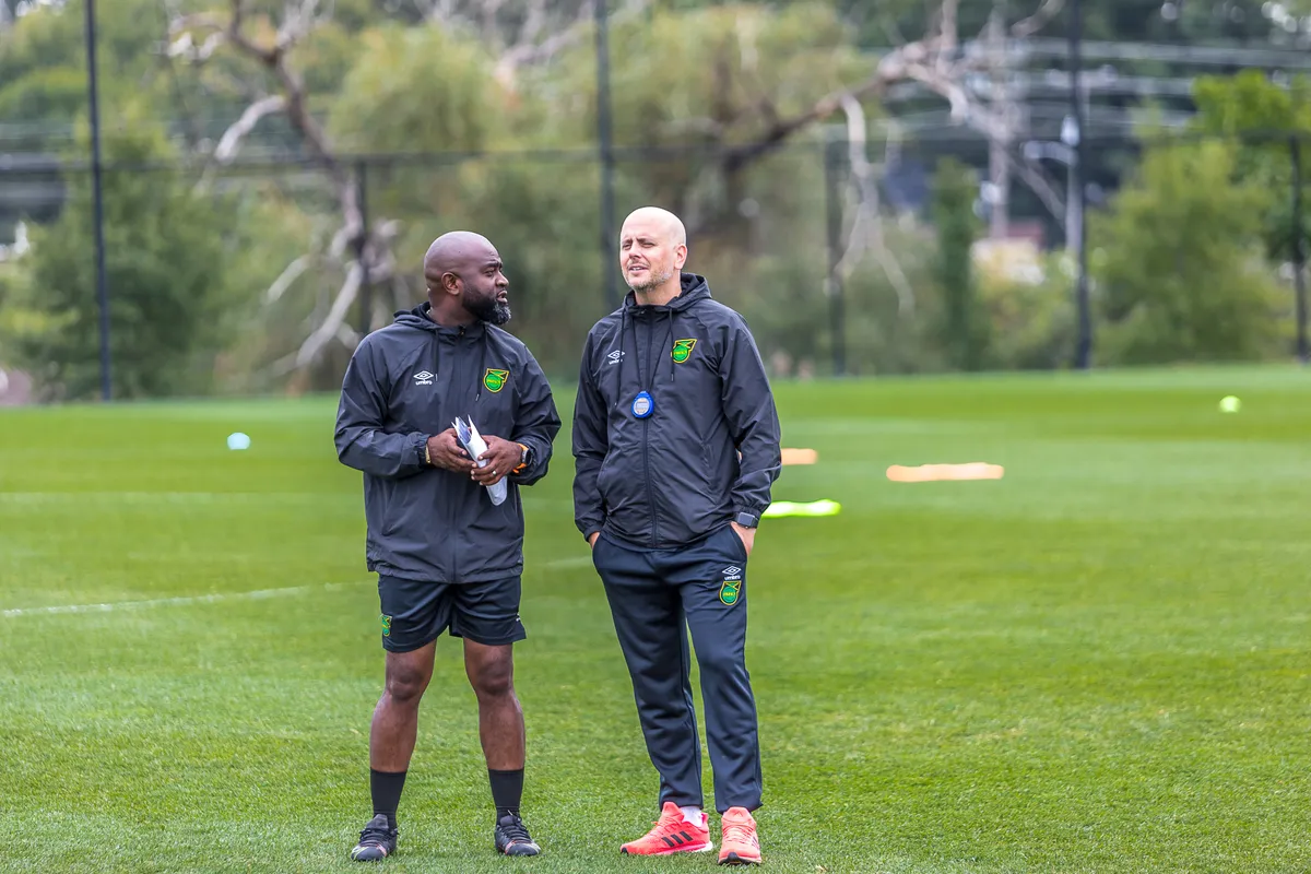 John Wall in Jamaica Football Federation kit talking with a fellow coach on the training pitch